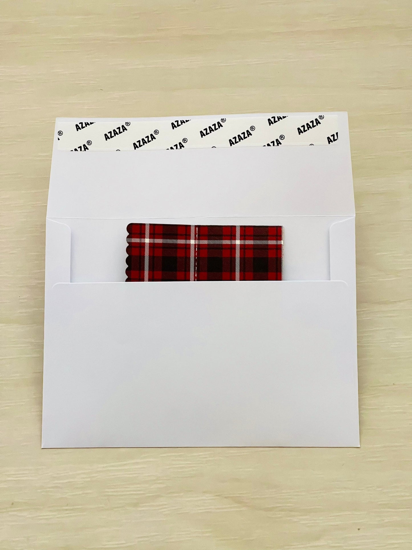 White envelope with a red and black plaid pop-up card folded inside on a wooden surface