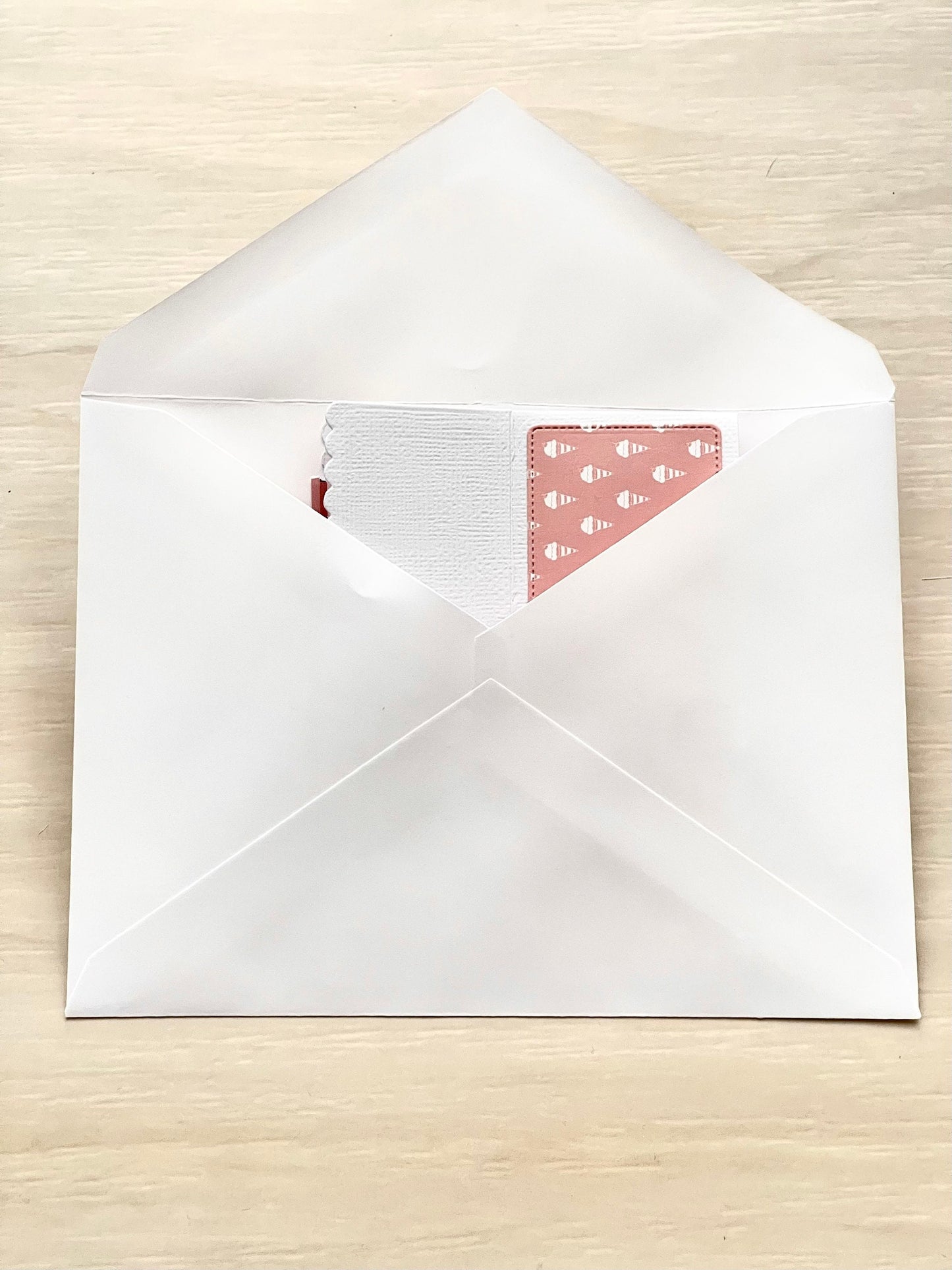 White envelope with a pink card featuring a pattern on a wooden surface