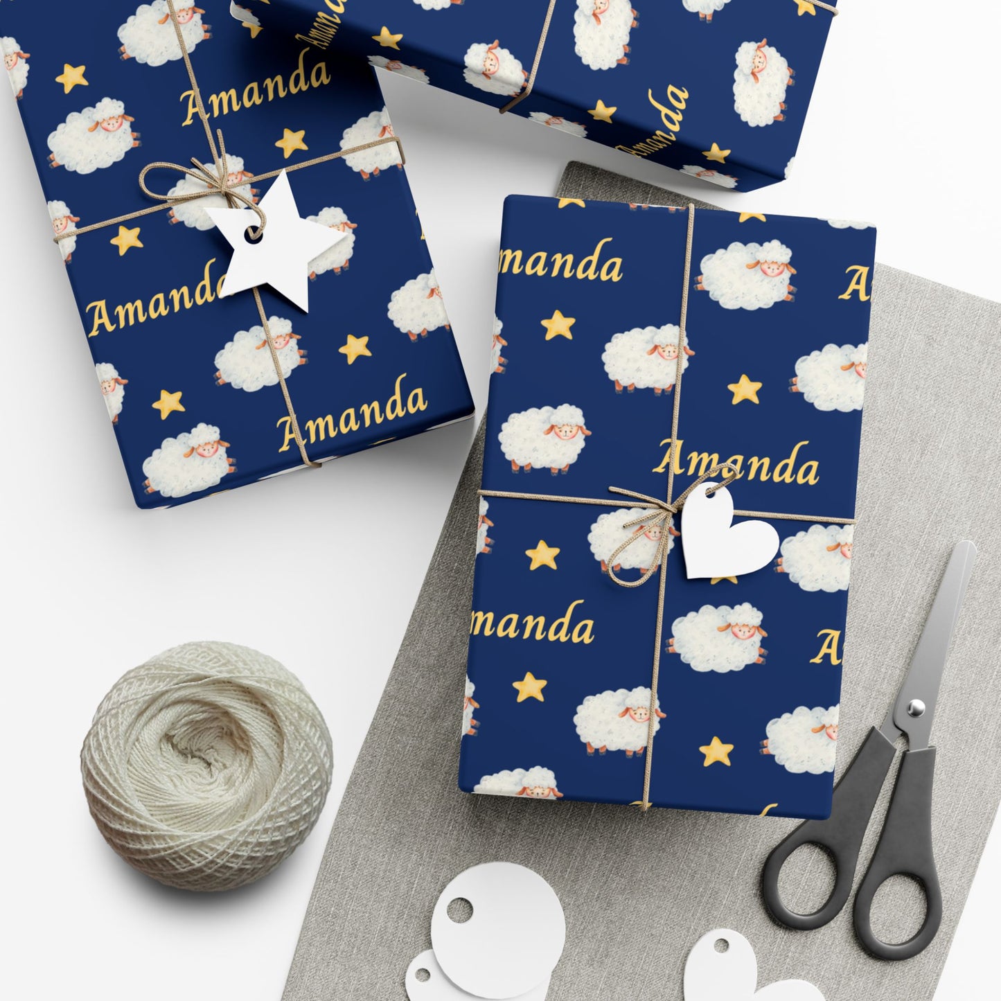 Personalized baby wrapping paper with navy blue background featuring watercolor sheep, stars, and a custom name printed throughout the design.