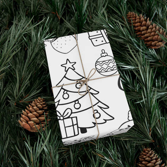 Gift wrapped in black and white patterned paper with Christmas elements made to be colored in, tied with brown string, on green pine needles with pine cones.