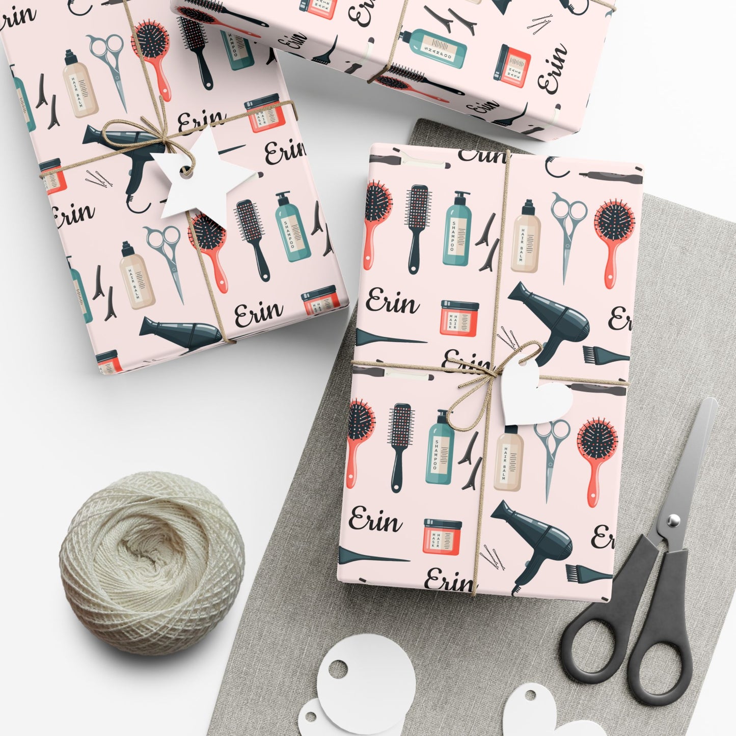 Gift boxes wrapped in hair salon-themed paper with scissors and yarn on a white surface