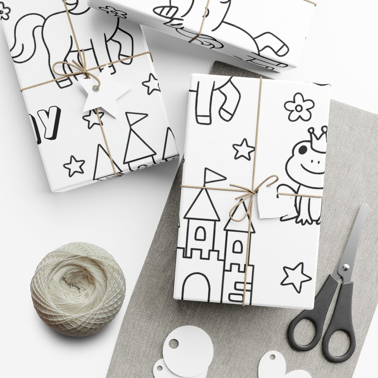 White gift wrap sheets with black princess themed line art for coloring in , tied with string, on a white surface with scissors and yarn.