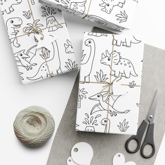 Two wrapped packages with dinosaur patterns, a ball of yarn, and scissors on a white surface.