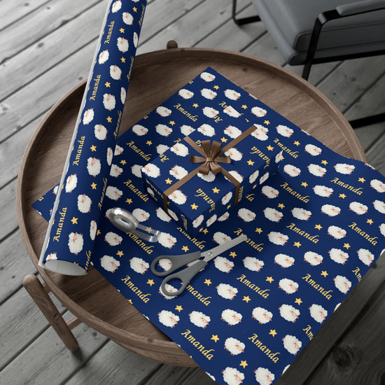 Blue gift wrap with white sheep pattern and 'Amanda' branding on a wooden surface.