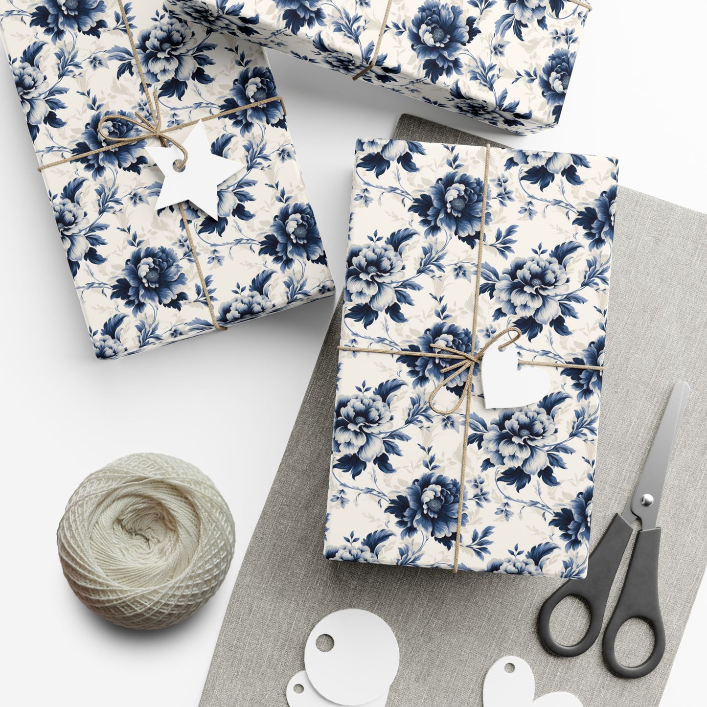 Gift boxes wrapped in blue floral paper with scissors and yarn on a white surface