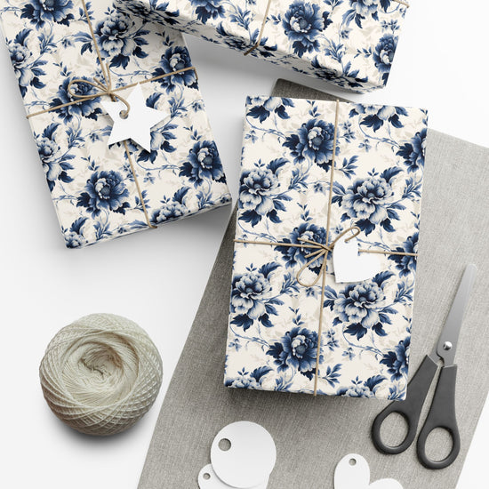 Gift boxes wrapped in blue floral paper with scissors and yarn on a white surface