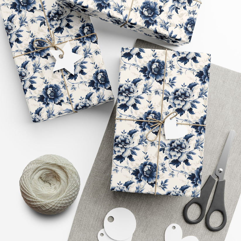 Gift boxes wrapped in blue floral paper with scissors and yarn on a white surface