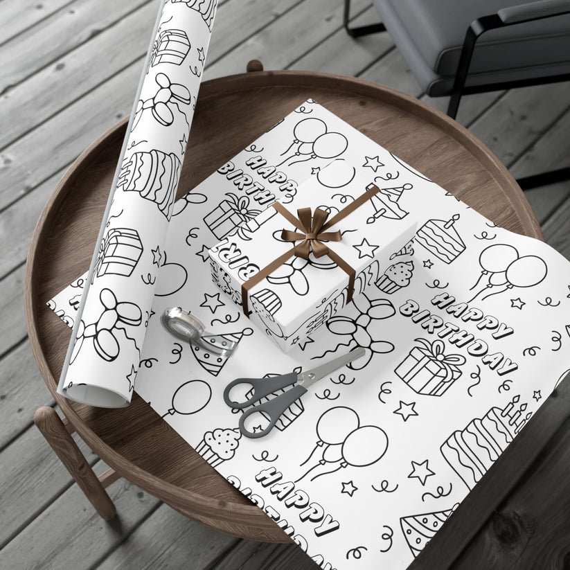 Roll of birthday-themed wrapping paper on a wooden table with a gift box.
