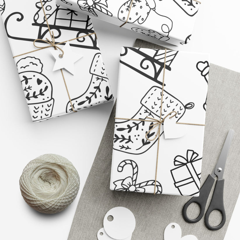 Gift wrap with black and white Christmas elements made for coloring in, scissors, and yarn on a white surface