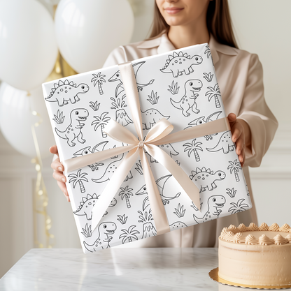 Person holding two wrapped presents with dinosaur patterns and a cake on a table.