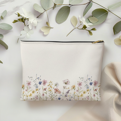 Off white pouch with floral design on a light background with green leaves