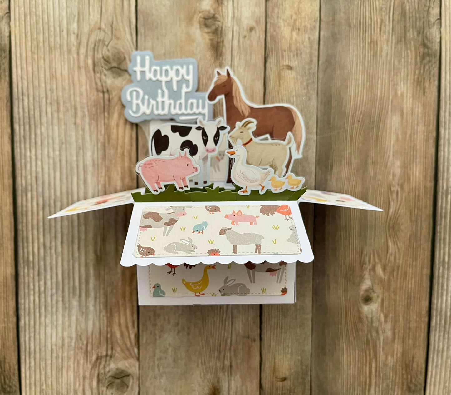 Pop-up birthday card with farm animal illustrations on a wooden background