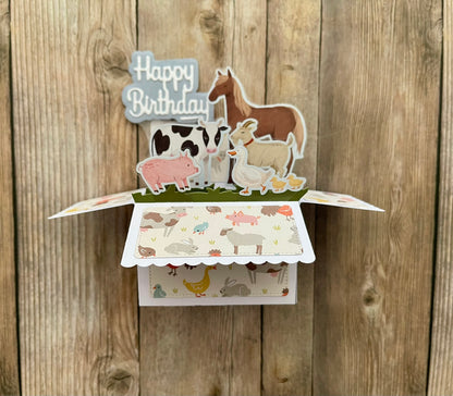 Pop-up birthday card with farm animal illustrations on a wooden background