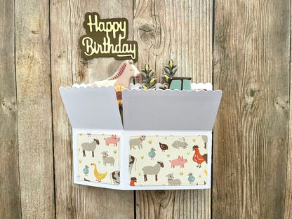 Folded box style pop-up birthday card with farm animal design on a wooden background