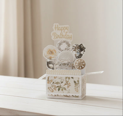 Pop-up birthday card with floral design and vintage masks on a wooden table.