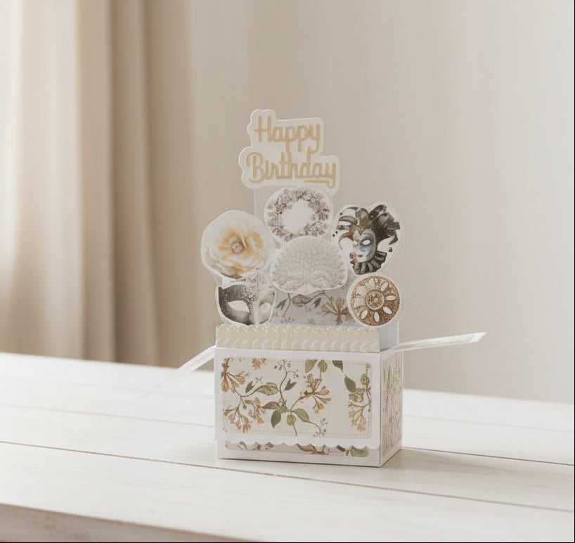 Pop-up birthday card with floral design and vintage masks on a wooden table.