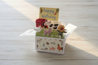 Pop-up birthday card with farm animals and 'happy birthday' sign on a dark surface