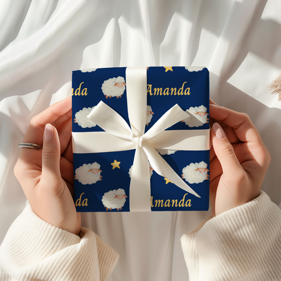 Personalized baby wrapping paper with navy blue background featuring watercolor sheep, stars, and a custom name printed throughout the design.
