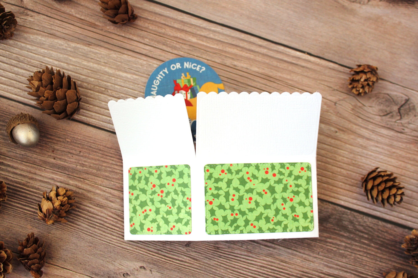 Folded pop-up card with mistletoe pattern on the back on a wooden surface with pine cones