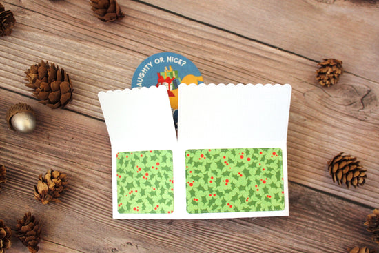Folded pop-up card with mistletoe pattern on the back on a wooden surface with pine cones