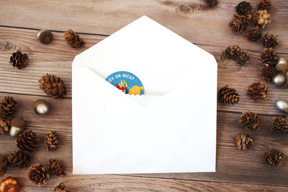 White envelope with a colorful sticker on a wooden surface with pine cones and small balls.