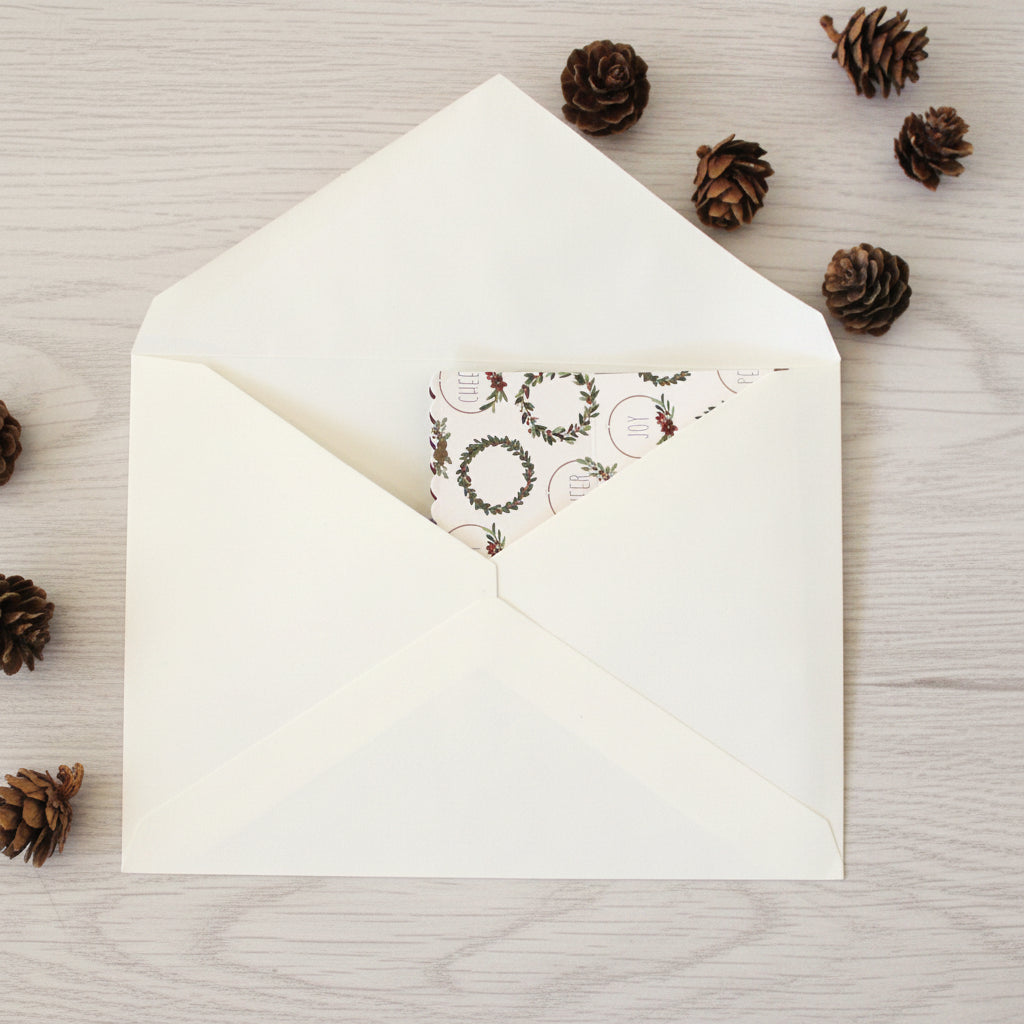 White envelope with a Christmas-themed card on a wooden surface with pine cones.