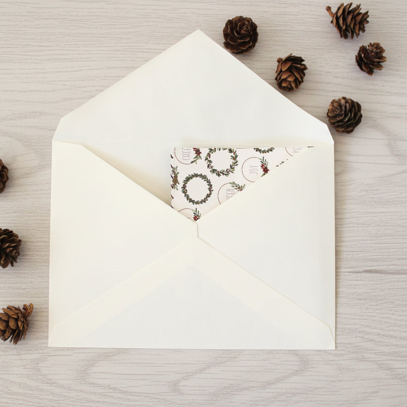 White envelope with a Christmas-themed card on a wooden surface with pine cones.