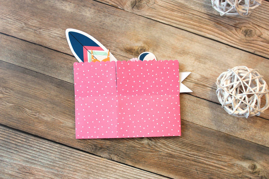 Pink paper wallet with white polka dots on a wooden surface