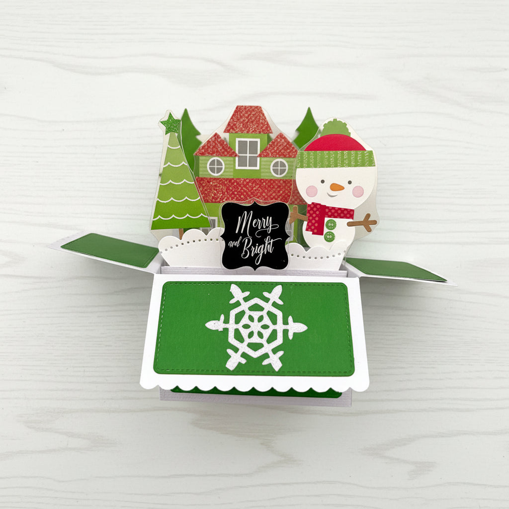 Christmas-themed pop-up card with snowman, trees, and house on a white background.