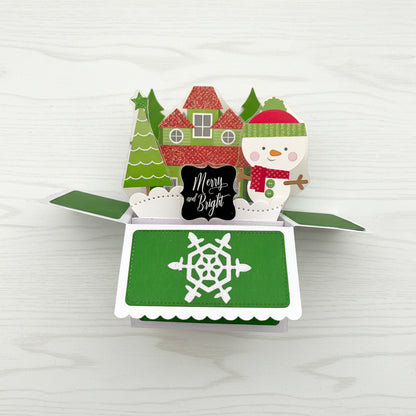Christmas-themed pop-up card with snowman, trees, and house on a white background.