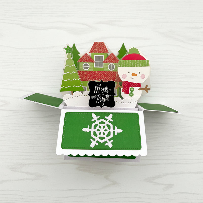 Christmas-themed pop-up card with snowman, trees, and house on a white background.