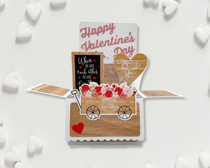 Valentine's Day card with a wooden cart, flowers, and decorative text on a white background.