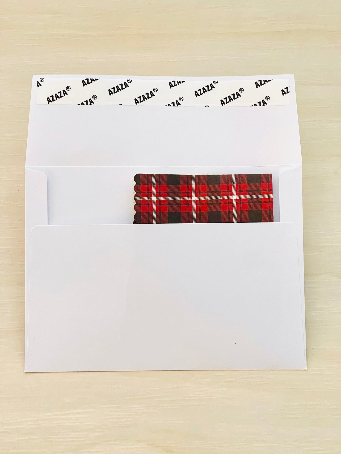 White envelope with a plaid patterned paper inside on a wooden surface