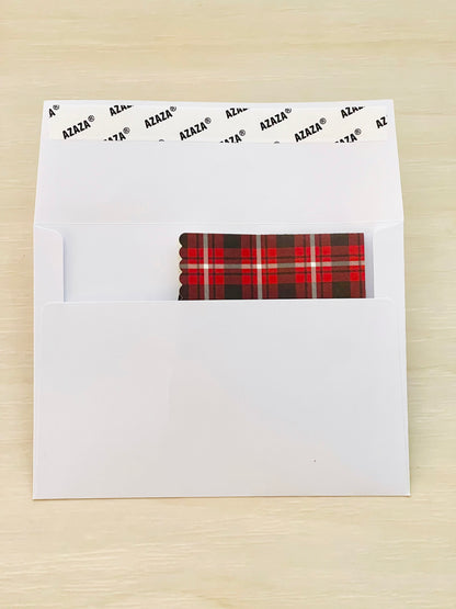 White envelope with a plaid patterned paper inside on a wooden surface