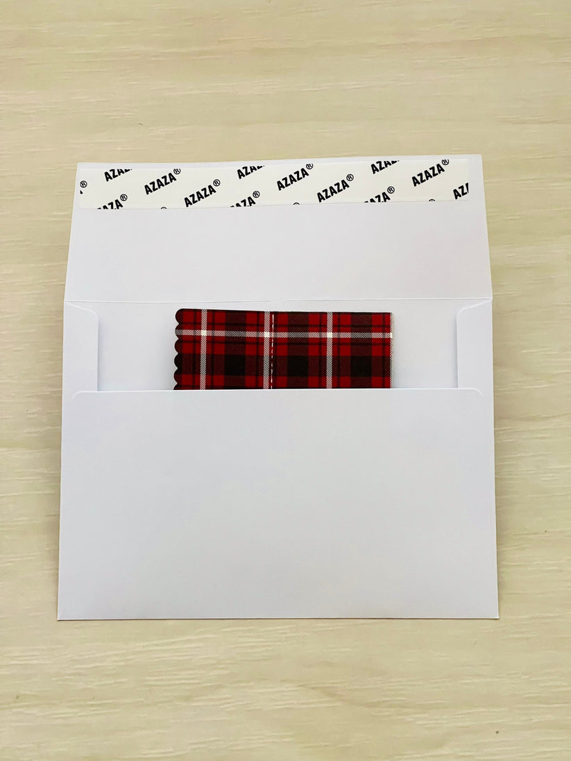 White envelope with a red and black plaid pop-up card folded inside on a wooden surface