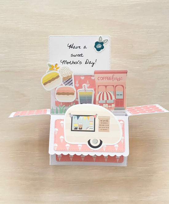 Pop-up card with coffeehouse-themed illustrations and 'Have a sweet Mother's Day!' text on a wooden surface.