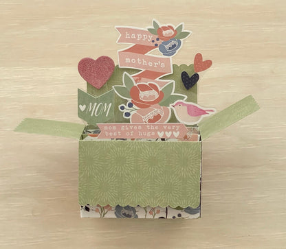 Decorative box pop-up card with floral patterns and text on a wooden surface