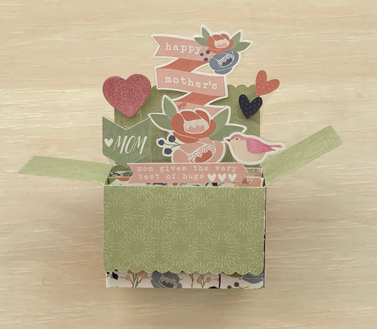 Decorative box pop-up card with floral patterns and text on a wooden surface
