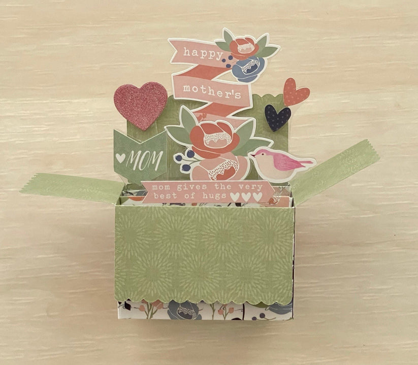 Decorative box pop-up card with floral patterns and text on a wooden surface