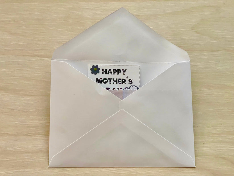White envelope with a 'Happy Mother's Day' card on a wooden surface