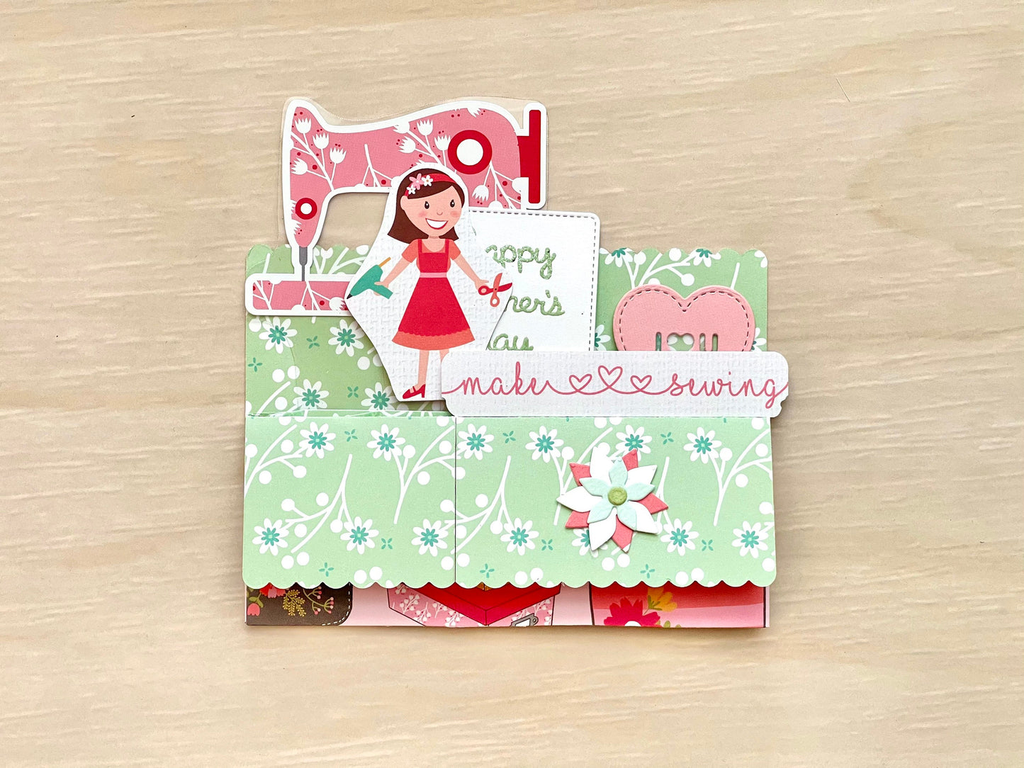 Card with sewing-themed design and cut-out figures on a wooden surface