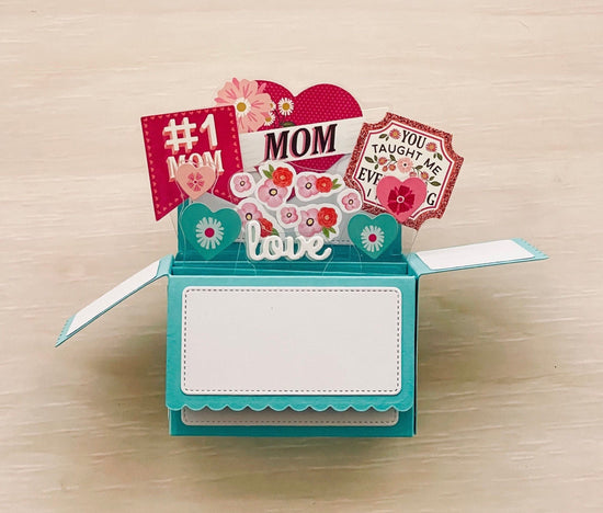 Pop-up card with 'Mom' text and floral designs on a wooden surface