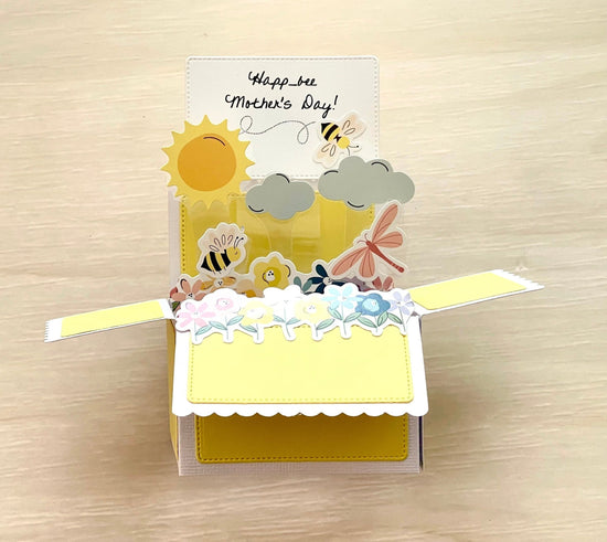 Pop-up card with 'Happy Mother's Day!' message and bee-themed design on a wooden surface