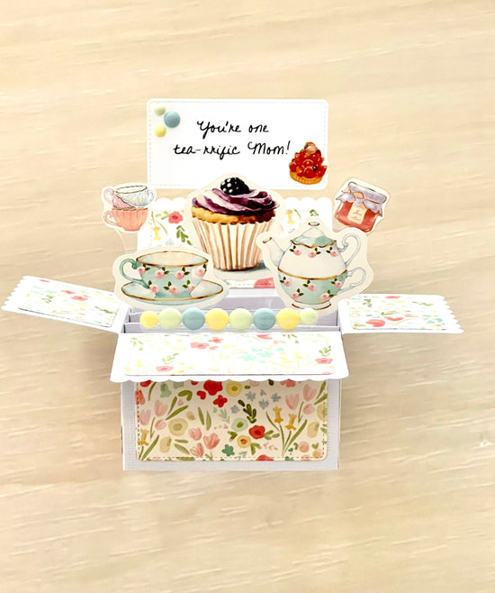 Decorative pop-up card with tea-themed illustrations on a wooden surface