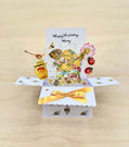 Pop-up birthday card with bees, flowers, and honey on a wooden surface