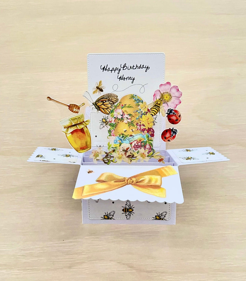 Pop-up birthday card with bees, flowers, and honey on a wooden surface