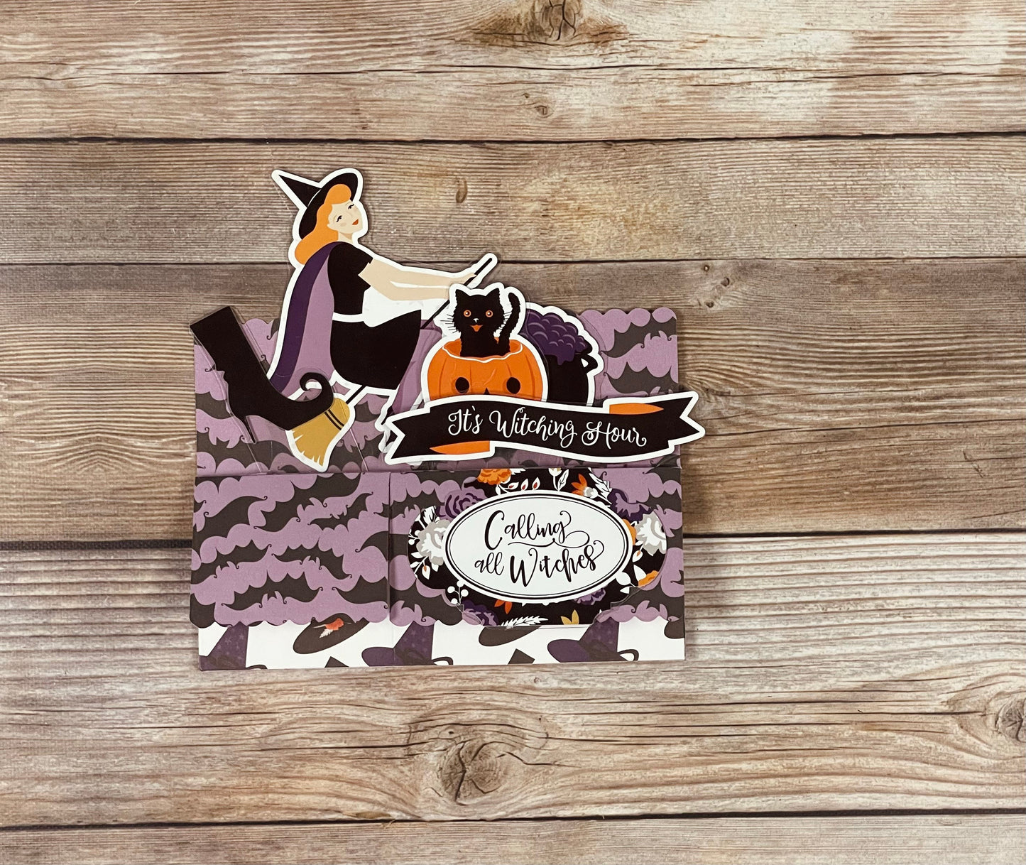 Halloween-themed card with a witch and cat design on a wooden surface