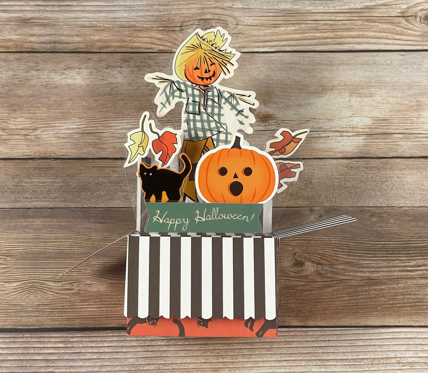 Halloween-themed card with a scarecrow, pumpkin, and black cat on a wooden background