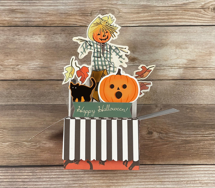 Halloween-themed card with a scarecrow, pumpkin, and black cat on a wooden background