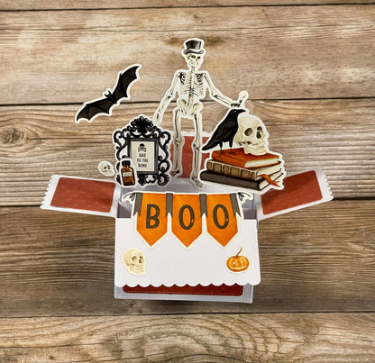 Halloween-themed pop-up card with skeleton, bat, and skull on a wooden surface